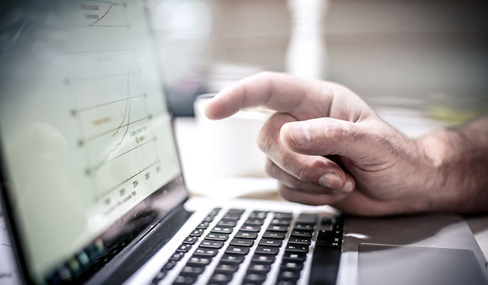 Close-up of a man's hand pointing at a laptop display of a graph
