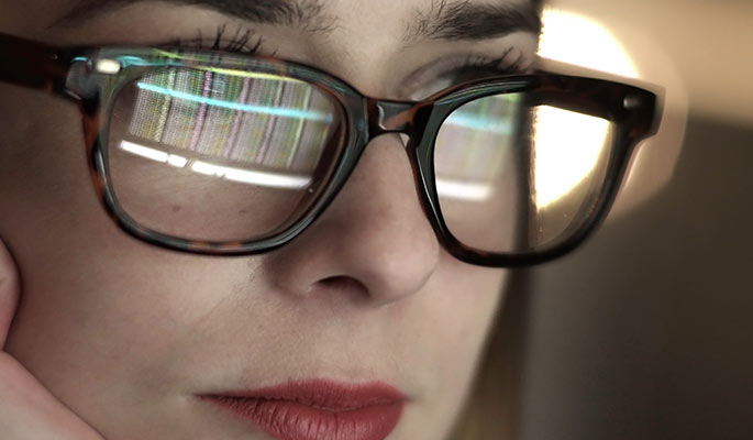 Close-up of a woman at a computer with graphs reflected in her glasses